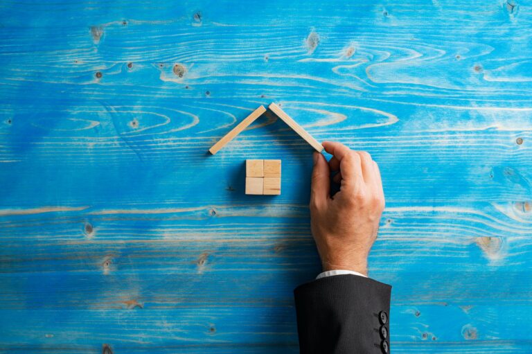 Top view of hand of a businessman or realtor building a house of wooden blocks